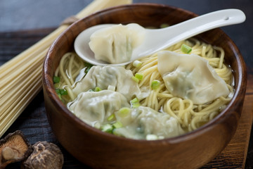 Wonton soup with egg noodles served in a wooden bowl, studio shot, close-up