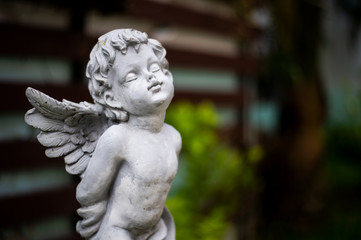 closeup cupid sculpture in garden with soft-focus and over light in the background
