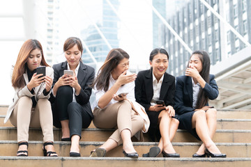 A group of working women in relaxing action. Some are talking and laughing each other, sitting together on steps and searching internet on mobile phone