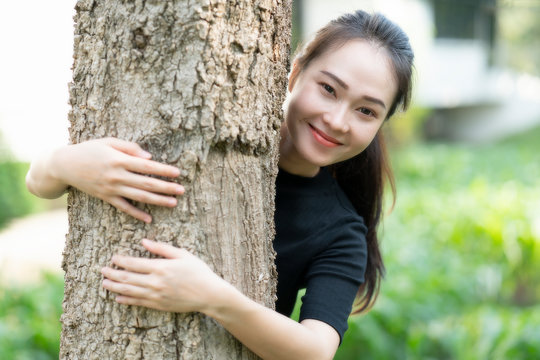 Close-up Of A Smiling Asian Young Woman Hugging Tree At The Park