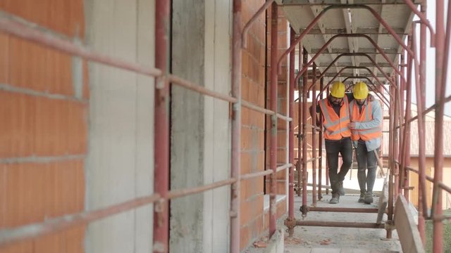 People working in construction site. Young men at work in new house inside apartment building. Latino manual worker helping injured co-worker after accident on duty