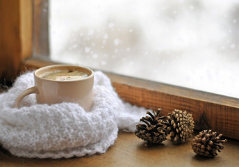Wooden winter window. A cup of hot coffee and a warm white knitted scarf on the windowsill. Still life