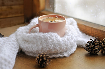 Wooden winter window. A cup of hot coffee and a warm white knitted scarf on the windowsill. Still life
