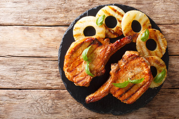 Main course: grilled pork chop steak in honey glaze with pineapples close-up on a slate plate....