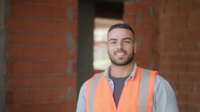 Proud people working in construction site. Portrait of happy white man at work in new house inside apartment building. Professional latino worker looking and smiling at camera