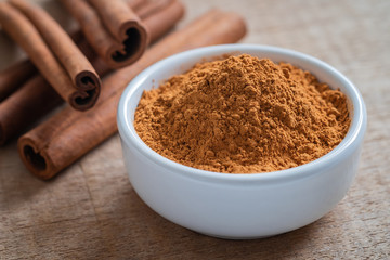 Cinnamon powder and cinnamon sticks on wooden table.
