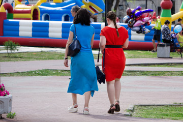 Back view of two friends walking together in a park at sunrise with a warm light in the background .