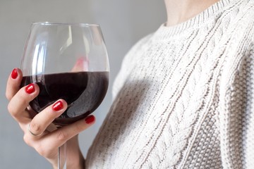 young woman with red nail polish wearing a beige sweater and holding a glass of red wine