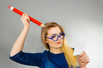 Confused woman holds big pencil note paper in hand