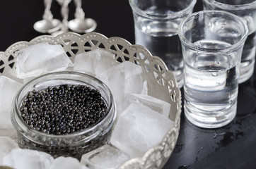 Black caviar  served in silver bowl with ice and vodka shots. European style caviar background.