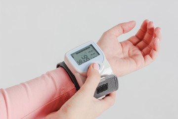 Tonometer device for measuring blood pressure on woman's hand on gray background isolated