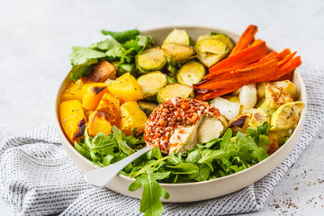 Baked brussels sprouts, zucchini, pumpkin, carrots and hummus salad in a white dish.