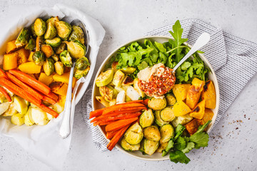 Baked brussels sprouts, zucchini, pumpkin, carrots and hummus salad in a white dish.