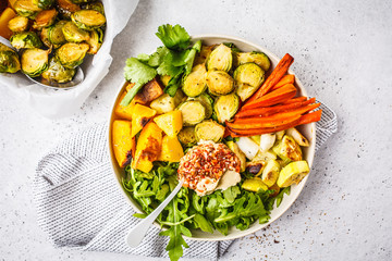 Baked brussels sprouts, zucchini, pumpkin, carrots and hummus salad in a white dish.
