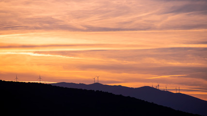 Side view of the silhouettes of mountain ranges at sunset time with wind generators on them. Greece