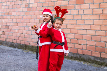 children dressed as santa claus with christmas balls and making ok symbol
