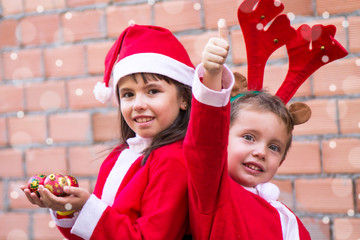 children dressed as santa claus with christmas balls and making ok symbol