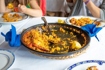 typical Spanish paella pan with seafood (squid), seashell (mussel, clam), rice and lemon with big spoon on white tablecloth of restaurant