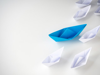 Blue paper boat leading among white ships