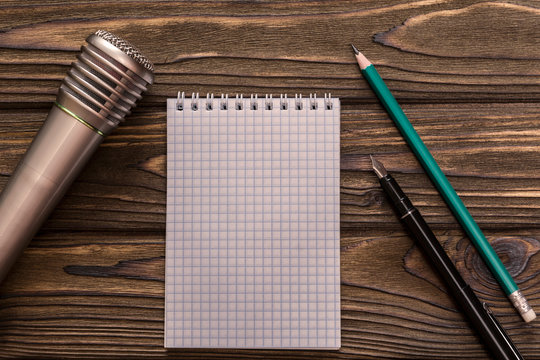 microphone, notebook, pen, pencil on the background of a wooden table. music creation, musical creativity, song writing.
