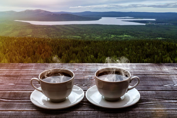two cups of coffee on a wooden table against a beautiful landscape with a lake and mountains covered with forests. romantic trip.