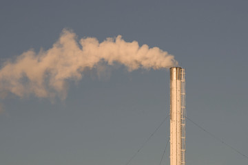 Industrial chimney steam factory on blue sky background. Air pollution, environmental disaster. Close-up view