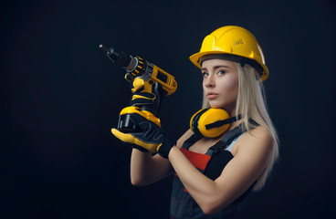 girl in construction clothes and protective equipment posing with a screwdriver