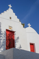 White Greek Orthodox church with a red door framed by the blue skies of Mykonos, Greece