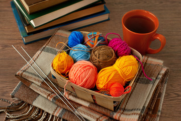 Knitting in a cozy atmosphere. A basket of yarn for knitting, a cup of tea, a book, a checkered...