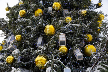 Decorated Christmas tree covered with snow. Natural christmas tree with yellow balls, gift boxes and toys. Snowy and happy Wintertime