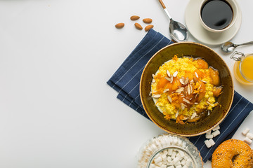 Oatmeal with baked fruit and nuts, fresh coffee, honey, bun and marshmallow on blue towel on white background, top view with empty space