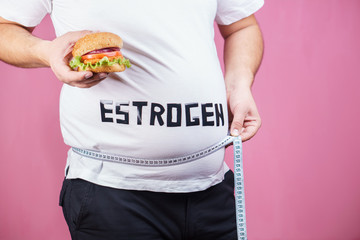 weight gain, fast food, hormonal imbalance, estrogen level. overweight man belly with hamburger and...