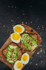 Fototapeta na wymiar Breakfast sandwich with avocado, egg on a rustic chopping Board. Healthy snack. Dark background, top view