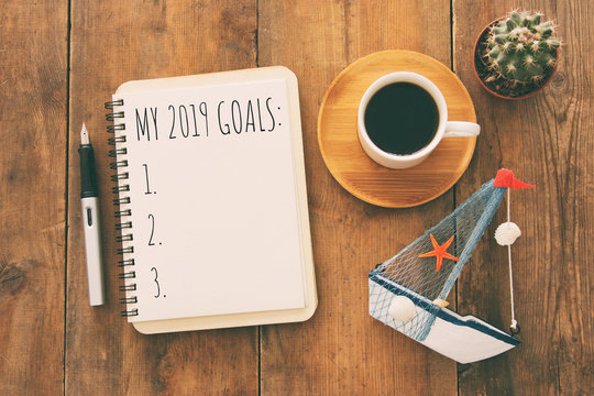 Top view image of 2019 goals list with notebook, cup of coffee over wooden desk.