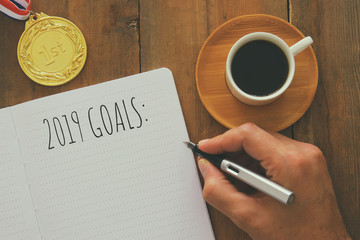 Top view image of 2019 goals list with notebook, cup of coffee over wooden desk.