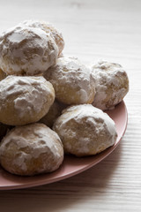Homemade white mexican wedding cookies on pink plate over white wooden surface, side view. Close-up.