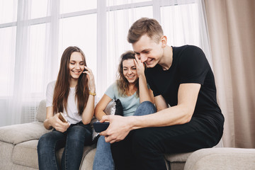 friendship, technology, happiness, leisure, social media, fun concept. Happy cheerful young people laughing watching video on smart phone at living room