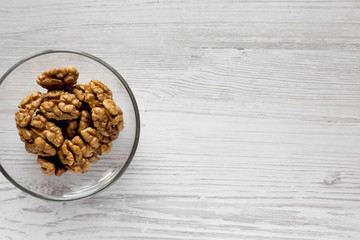 Walnuts in glass bowl on white wooden background, overhead view. Flat lay, from above. Copy space.