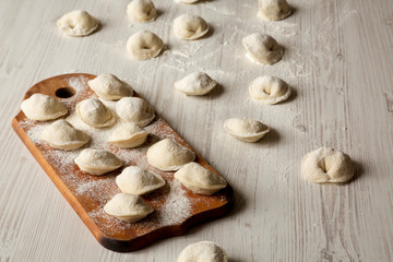 Homemade raw tortellini on white wooden surface, low angle view.