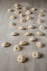 Homemade raw tortellini on white wooden background, low angle view.