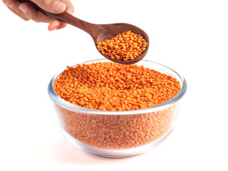 Yellow lentil in glass bowl with wooden spoon in the hand isolated on white background.