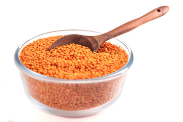 Yellow lentil in glass bowl with wooden spoon isolated on white background