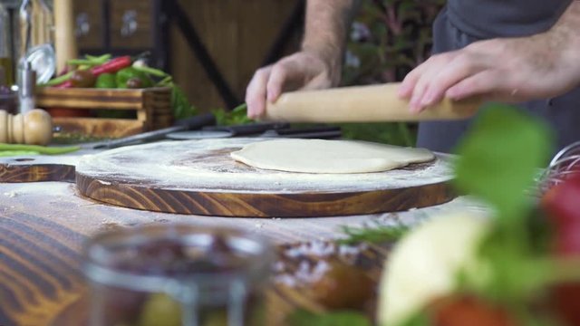 Rolling dough with rolling pin for pizza preparation on table. Chef hands rolling dough for pie with wooden roller. Baking bread and cake in bakery. Chef cook cooking food on kitchen table.
