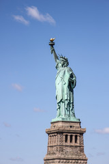 Fototapeta na wymiar Statue of Liberty near New York city and Manhattan taken from a boat with a beautiful blue sky and some clouds in the background, United States