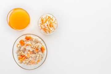 Oatmeal with pumpkin and nuts, salad and a glass of fresh juice on a white background. Top view Copy space.