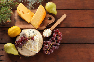 Various type of cheese and fruits on wooden boards and Christmas tree twigs. Swiss cheese, blue cheese, camembert and cottage cheese for Christmas. Dairy products, lemon, grapes and pears. Top view