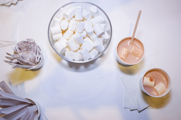 flat lay On a white tabletop in a glass marshmallow cup, two cups of cocoa