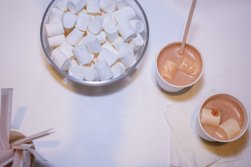 flat lay On a white tabletop in a glass marshmallow cup, two cups of cocoa