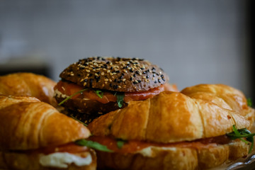 Close-up of a glass tray on a thin leg, on which are sandwiches with ham, tomatoes and greens.