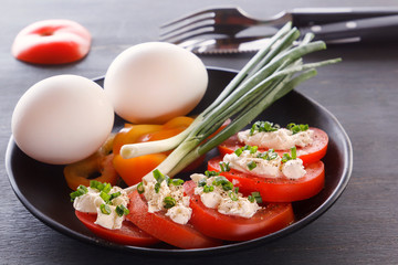 Sliced tomatoes with cheese and herbs in a black plate with onions, sweet peppers and eggs. Close-up